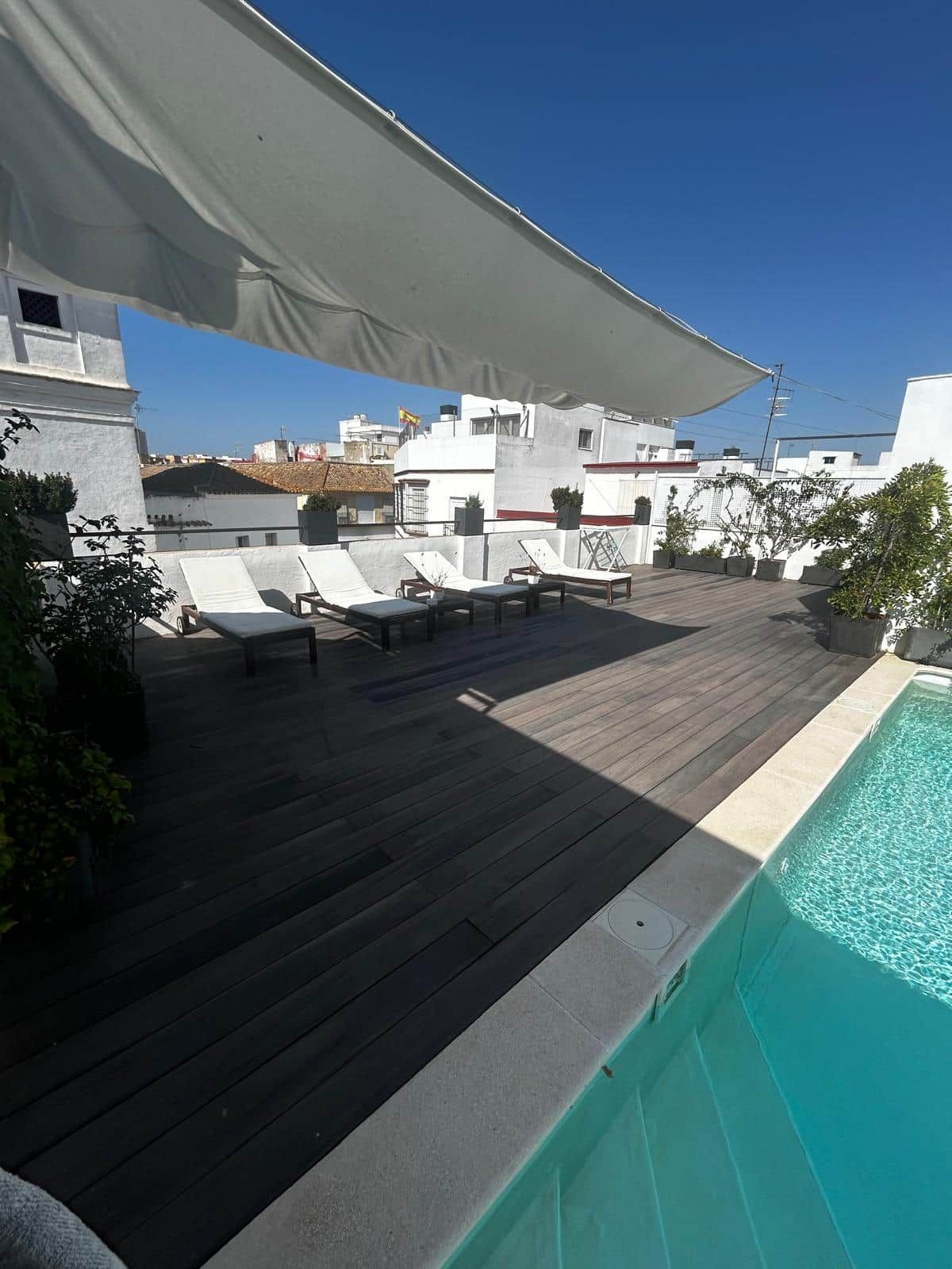 A rooftop terrace with a swimming pool, lounge chairs, and a large white awning.
