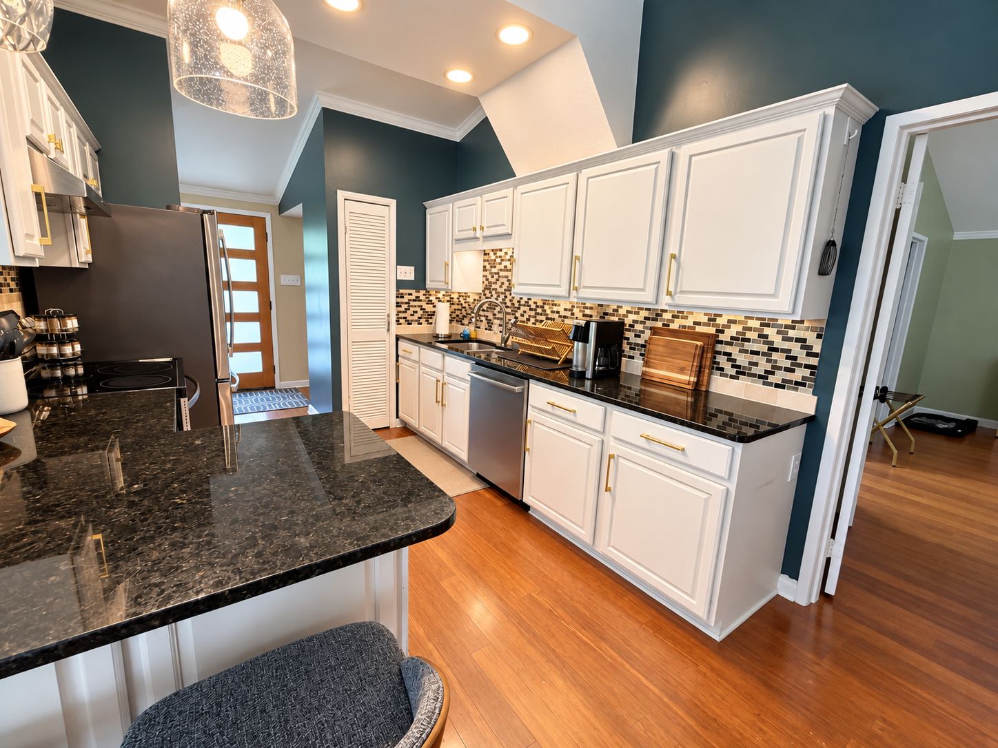Una cocina moderna con armarios blancos, encimera de granito negro y salpicadero con un diseño de mosaico.