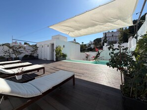 Une terrasse sur le toit avec des chaises longues, une piscine et un bâtiment blanc en arrière-plan.
