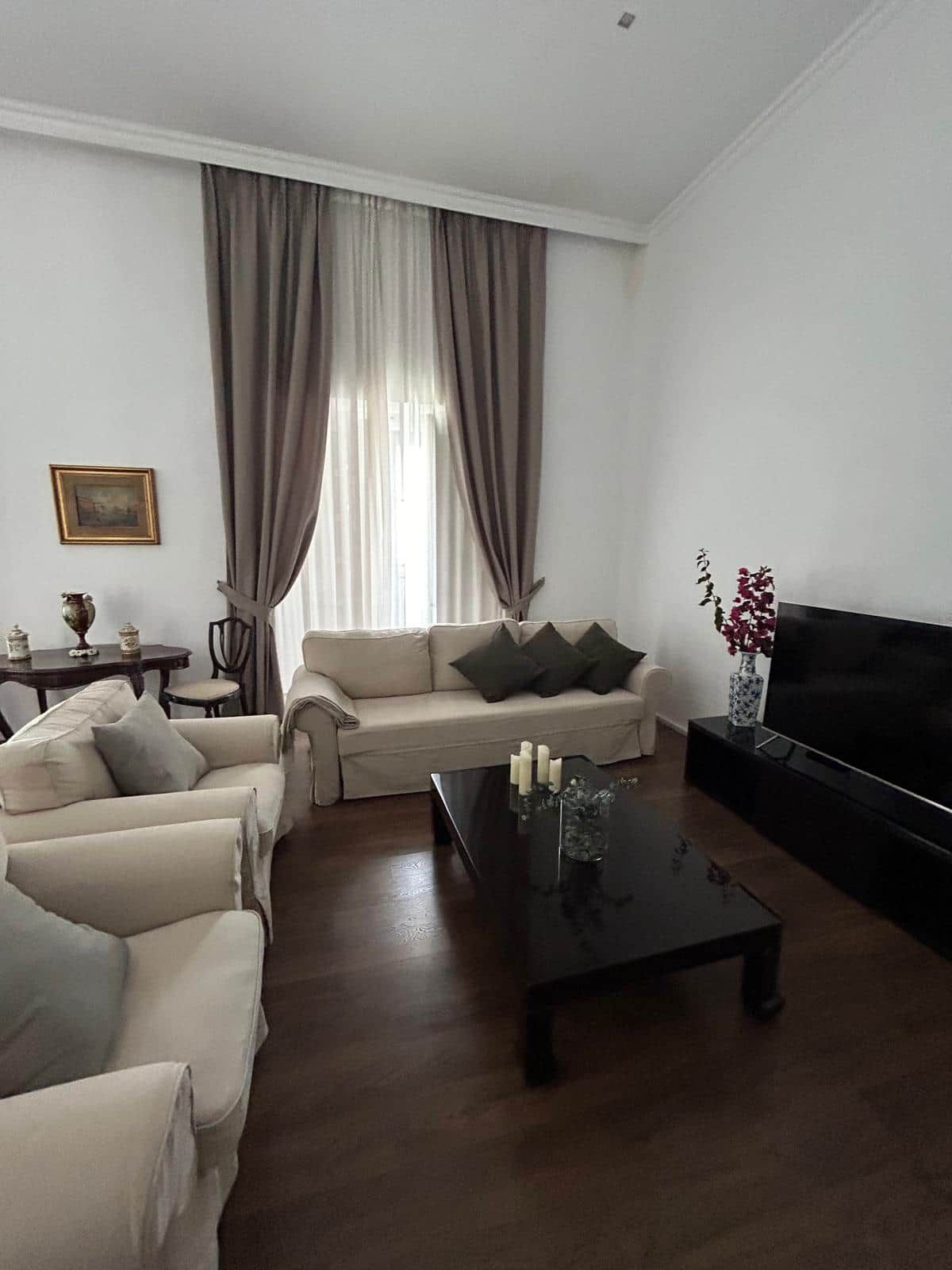 A living room with a sofa, a coffee table, a TV, and a window with curtains.
