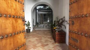 Un couloir au sol orné d’un motif en chevrons, bordé de portes en bois rehaussées de clous en métal, qui mène à une porte en arc de cercle.