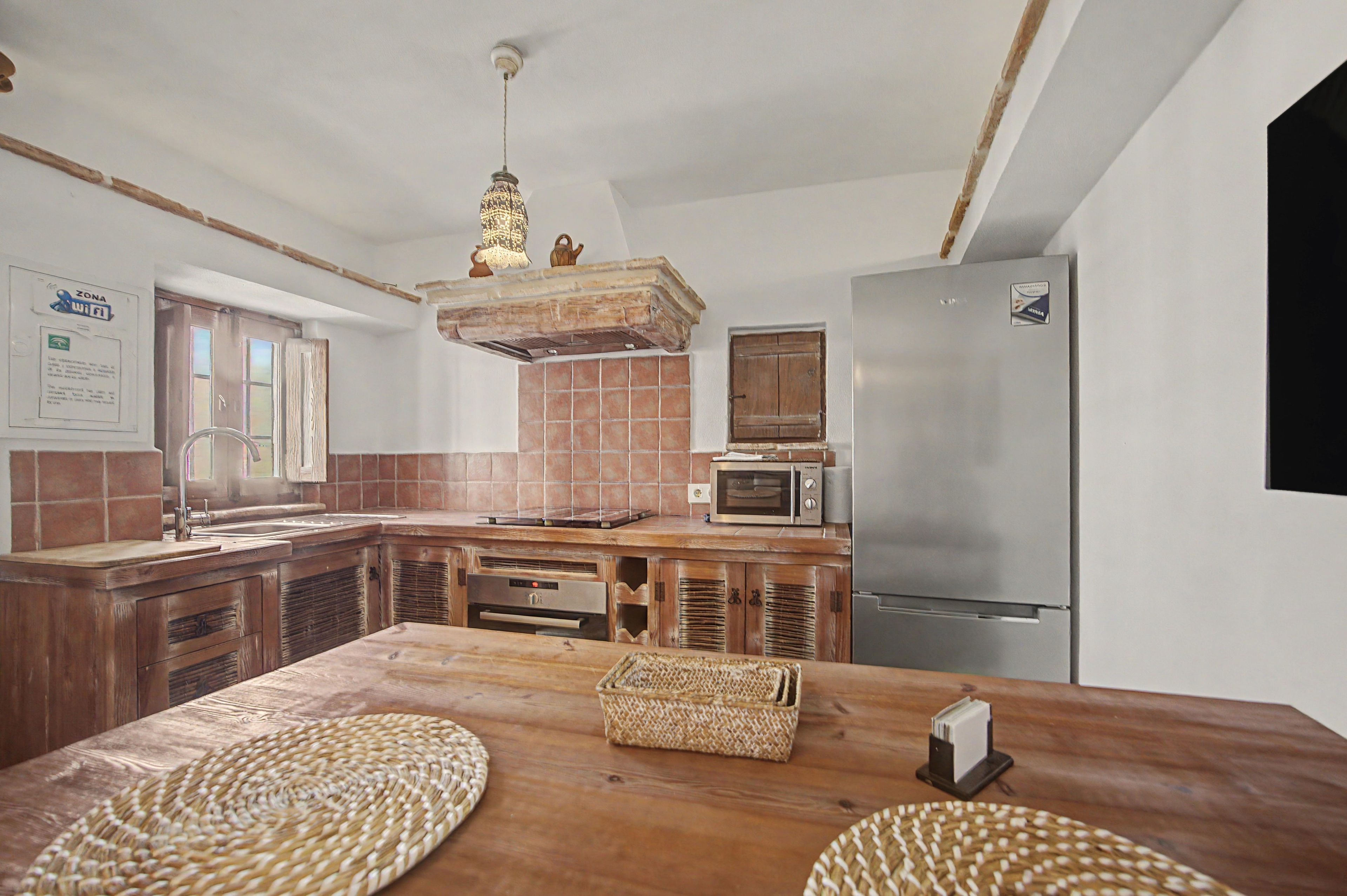 A kitchen with a wooden table, a microwave, a refrigerator, and a hanging light fixture.