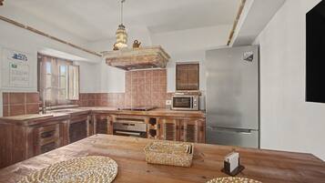 A kitchen with a wooden table, a microwave, a refrigerator, and a hanging light fixture.