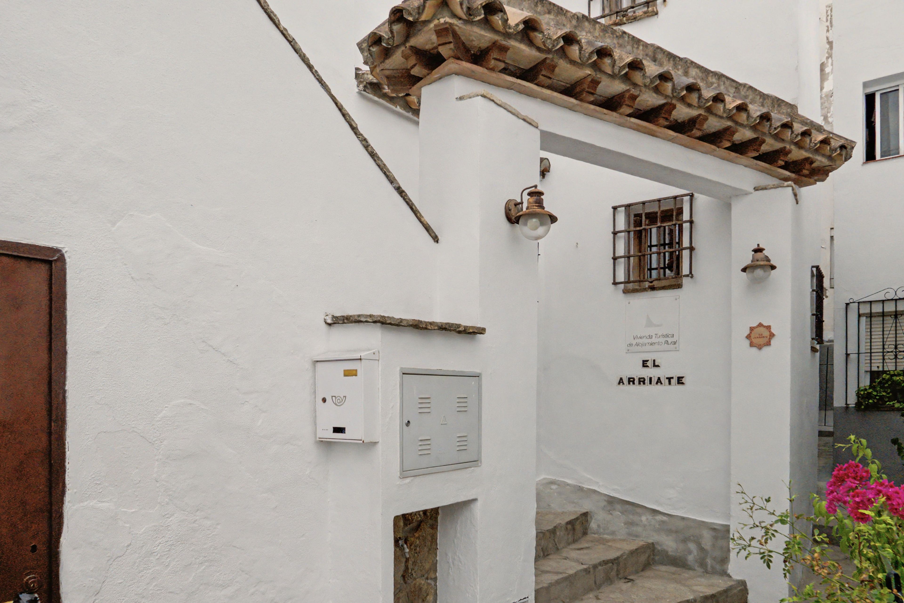 Una calle estrecha con un edificio blanco, una puerta de madera y un letrero que dice 'EL ARRIATE'.