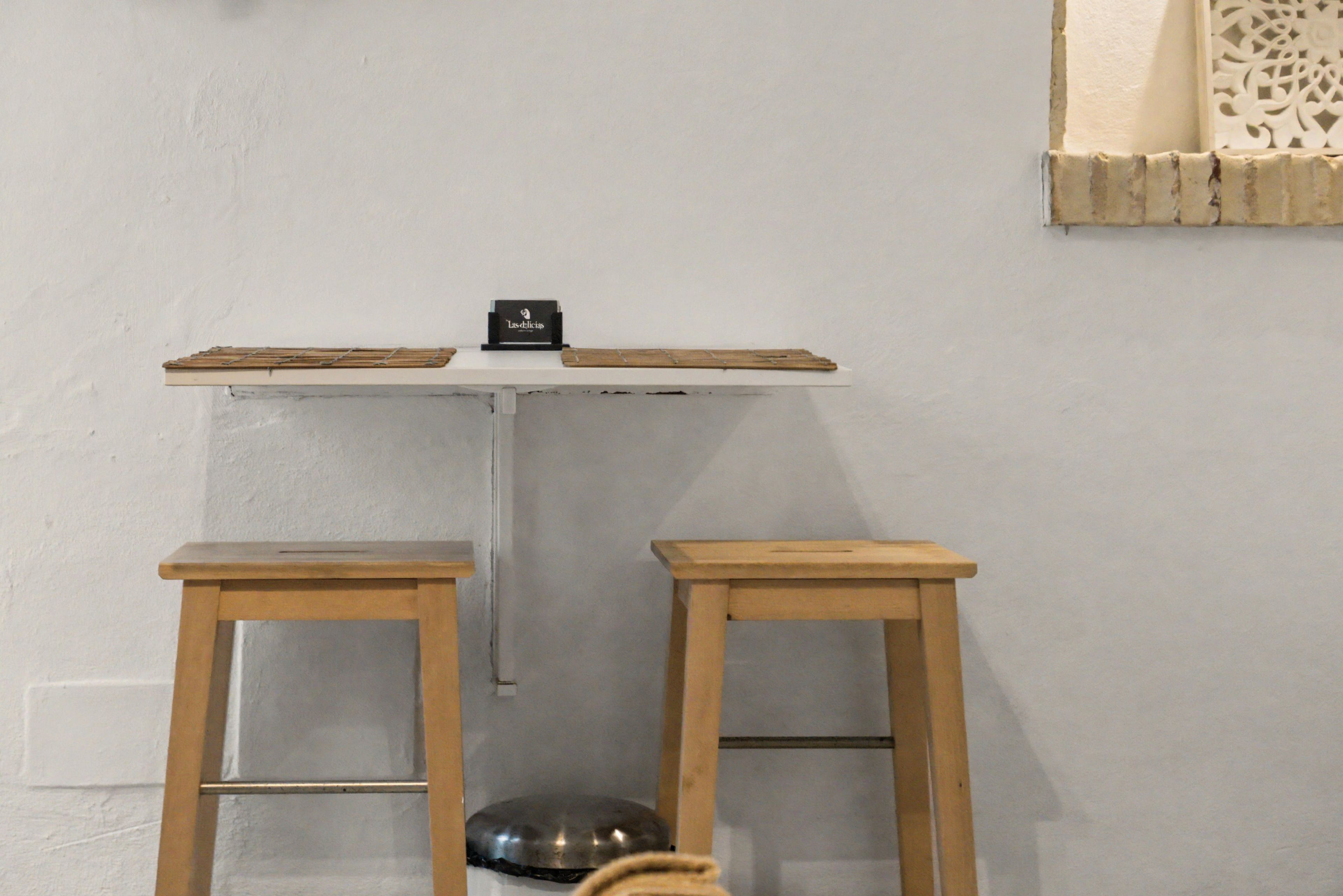 Una habitación pequeña con pared blanca, una estantería con un objeto negro y dos taburetes de madera.