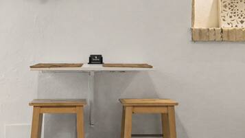 Una habitación pequeña con pared blanca, una estantería con un objeto negro y dos taburetes de madera.