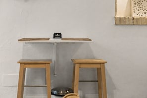 Una habitación pequeña con pared blanca, una estantería con un objeto negro y dos taburetes de madera.