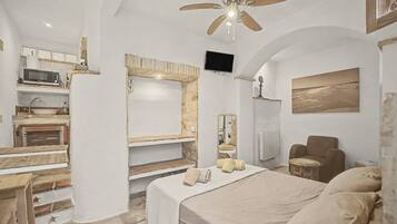 Un dormitorio con cama, una silla, televisor y ventilador de techo.