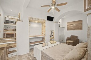 Une chambre à coucher avec un lit, une chaise, un téléviseur et un ventilateur de plafond.