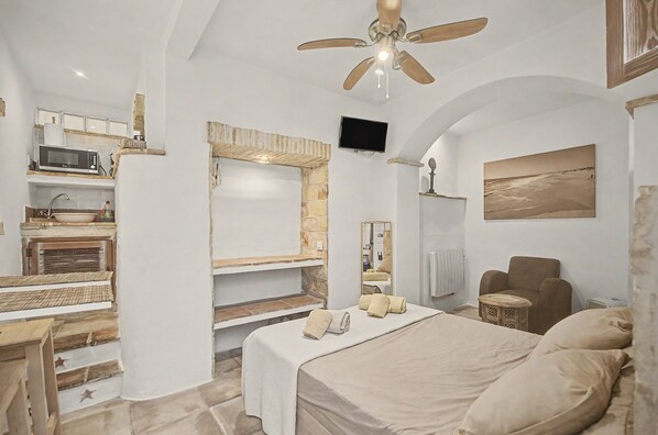 Un dormitorio con cama, una silla, televisor y ventilador de techo.