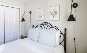 Un dormitorio con una cama, dos lámparas de pared y dos láminas botánicas enmarcadas.