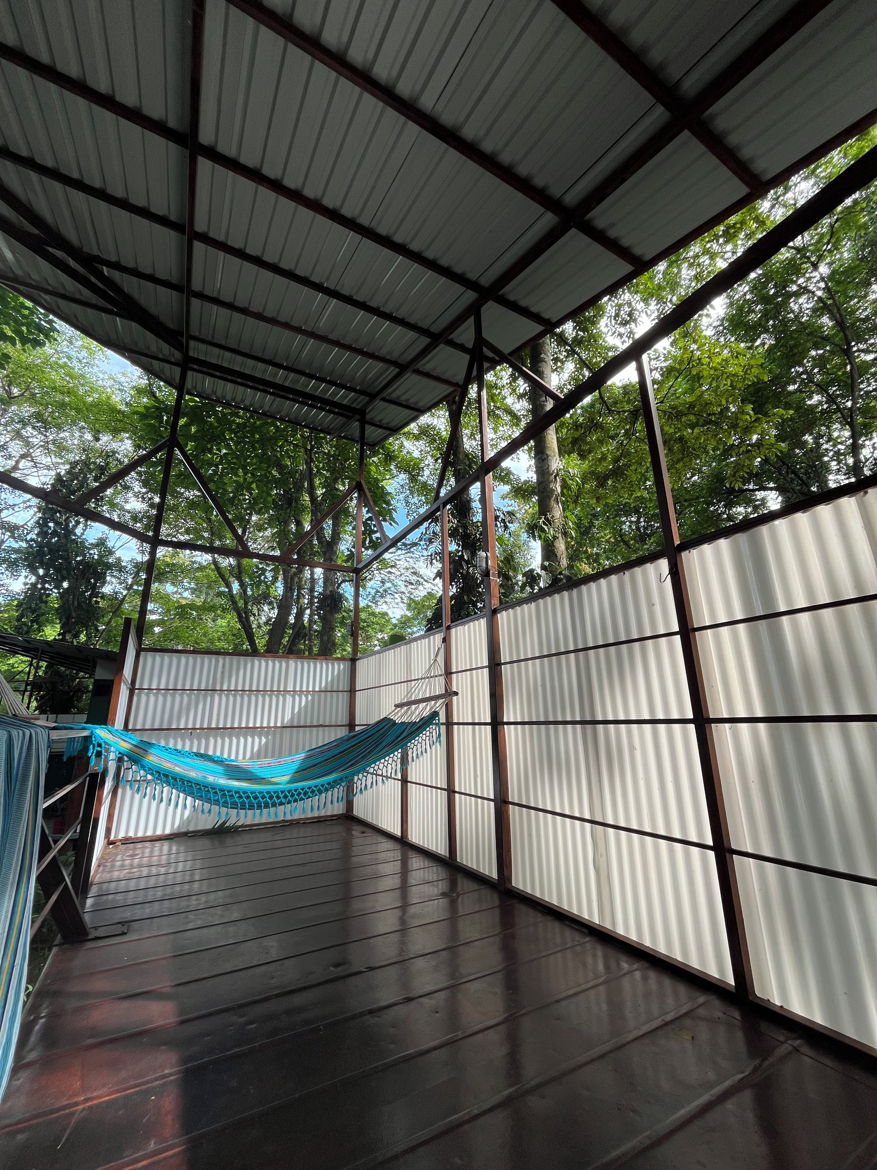 A covered outdoor area with a hammock, metal walls, and a view of trees.