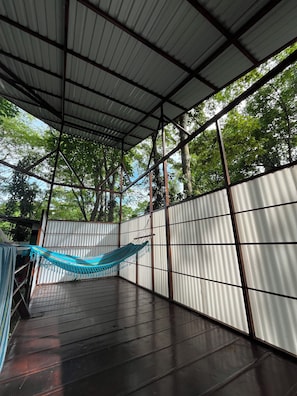 A covered outdoor area with a hammock, metal walls, and a view of trees. - Villa Keköl - Casa Numa (Puerto Viejo de Talamanca)