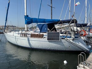 A sailboat docked at a marina with a blue tarp on deck, a life buoy, and a solar panel.