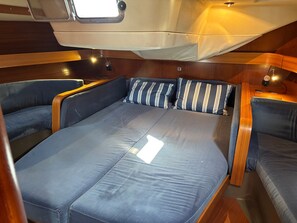 A compact, well-lit interior with a central bed, two seating areas with cushions, and a small table. - Spend the Night on a Sailboat in Lagos (Lagos)