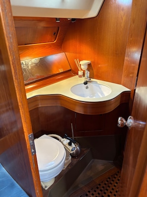 A compact bathroom with a wooden vanity, a sink, and a toilet. - Spend the Night on a Sailboat in Lagos (Lagos)