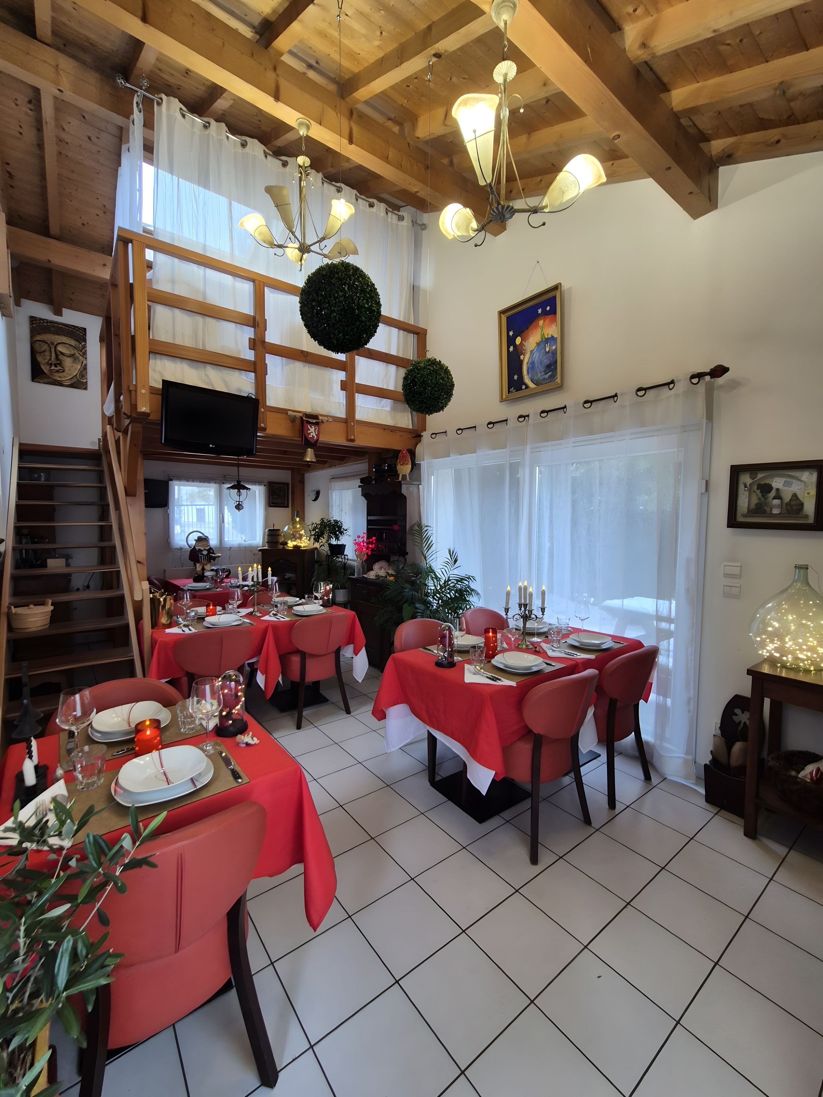 Un coin repas avec des nappes rouges, des poutres en bois et un téléviseur fixé au mur.
