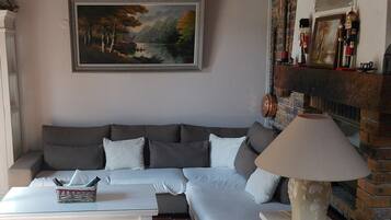 Een woonkamer met een bank, een salontafel, een lamp, een open haard en een schilderij aan de muur.