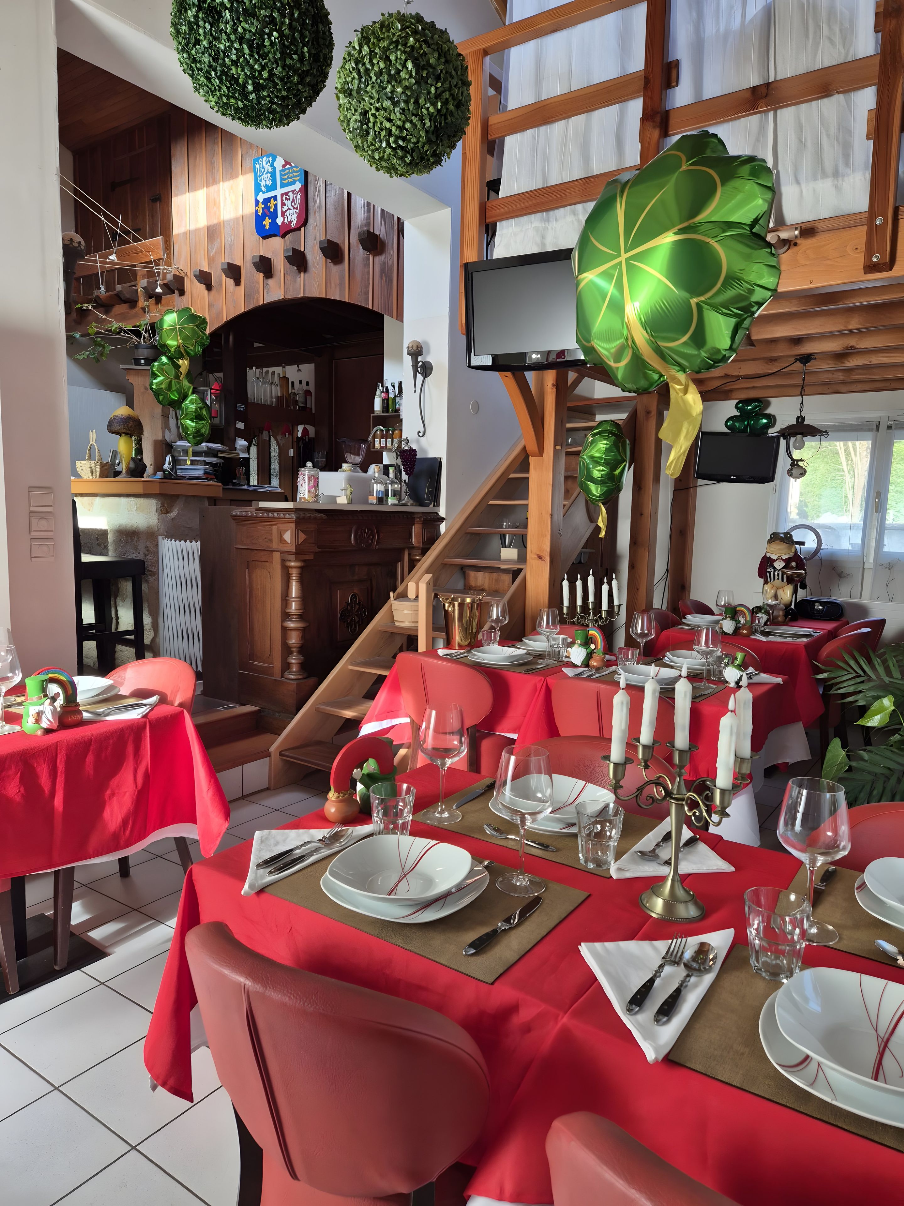 A restaurant with red tablecloths, white candles, and a wooden staircase.