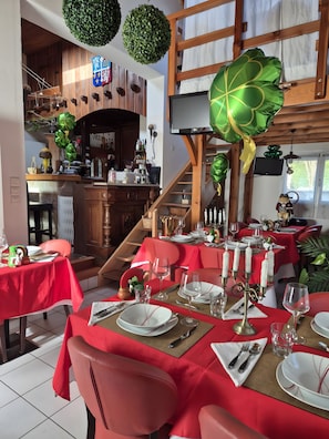 A restaurant with red tablecloths, white candles, and a wooden staircase.