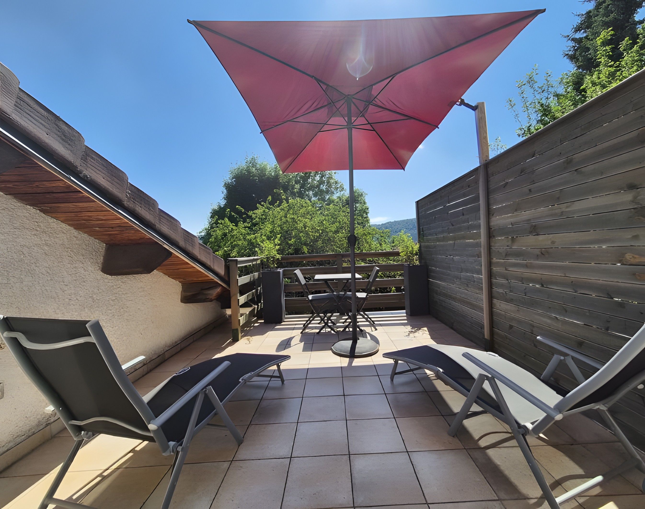 Un espace patio avec une table et des chaises, un parasol rouge et une clôture en bois.