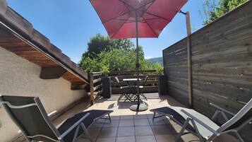 Un espace patio avec une table et des chaises, un parasol rouge et une clôture en bois.