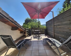 A patio area with a table and chairs, a red umbrella, and a wooden fence.