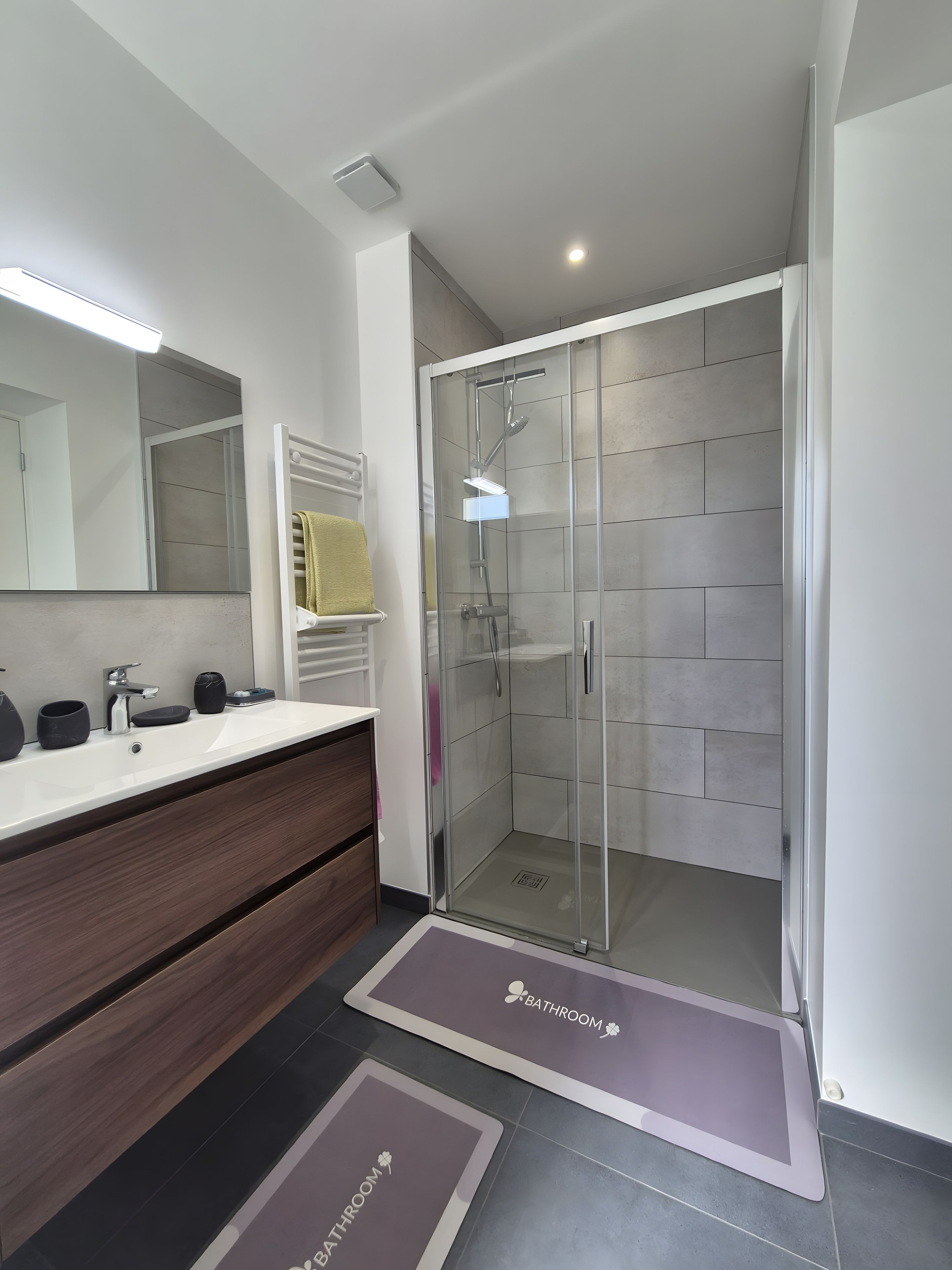 Een moderne badkamer met een douchecabine van glas, een wastafel met spiegel en een wasbak.