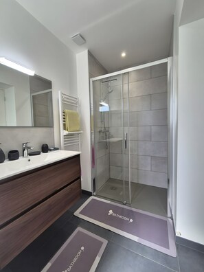 Un baño moderno con ducha envuelta en vidrio, tocador con espejo y lavamanos.