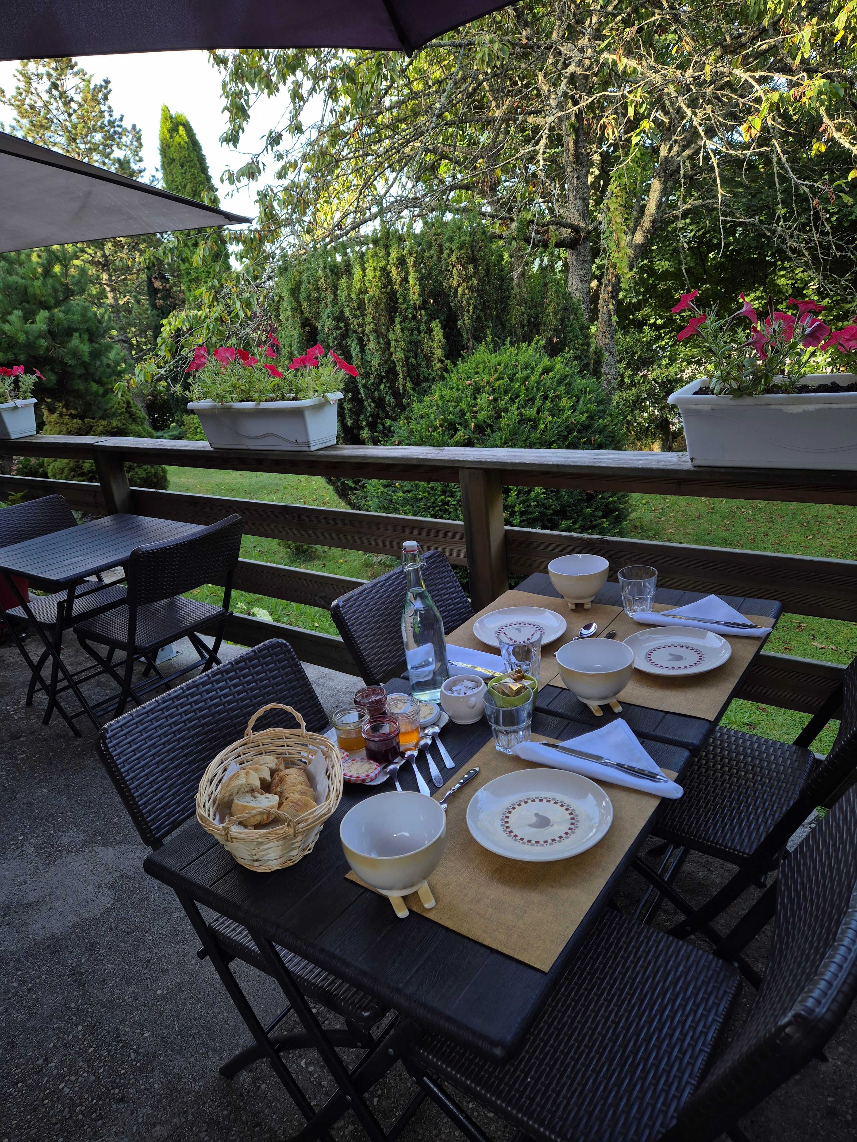 Un espace extérieur aménagé pour les repas, avec une table dressée pour quatre personnes, entourée de chaises, agrémenté de plantes en pot et doté d’une terrasse en bois.