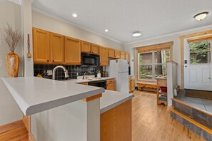 A modern kitchen with wooden cabinets, a stainless steel range, and a large island with a sink. - New 2-bedroom townhome with private hot tub (Silverthorne)