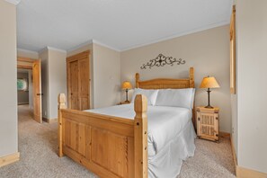 A bedroom with a wooden bed, two bedside tables with lamps, a door, and a decorative wall piece. - New 2-bedroom townhome with private hot tub (Silverthorne)