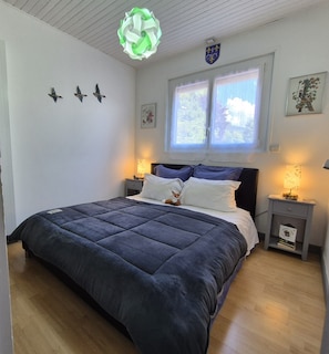 Un dormitori amb un llit gran, dues taules de nit, una finestra amb cortines i decoracions de pássars penjades a la paret.