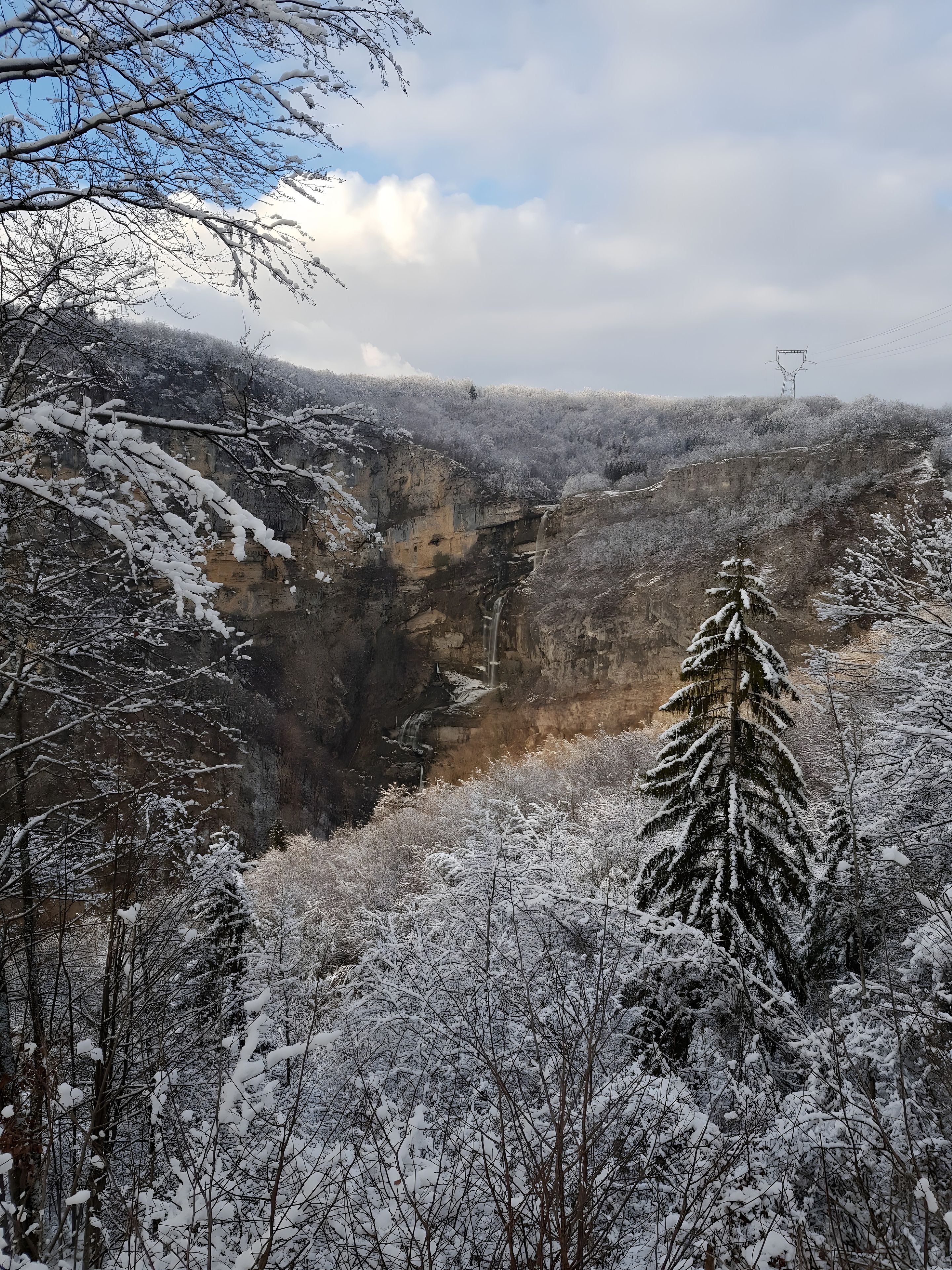 A snowy landscape with a waterfall and forested area.