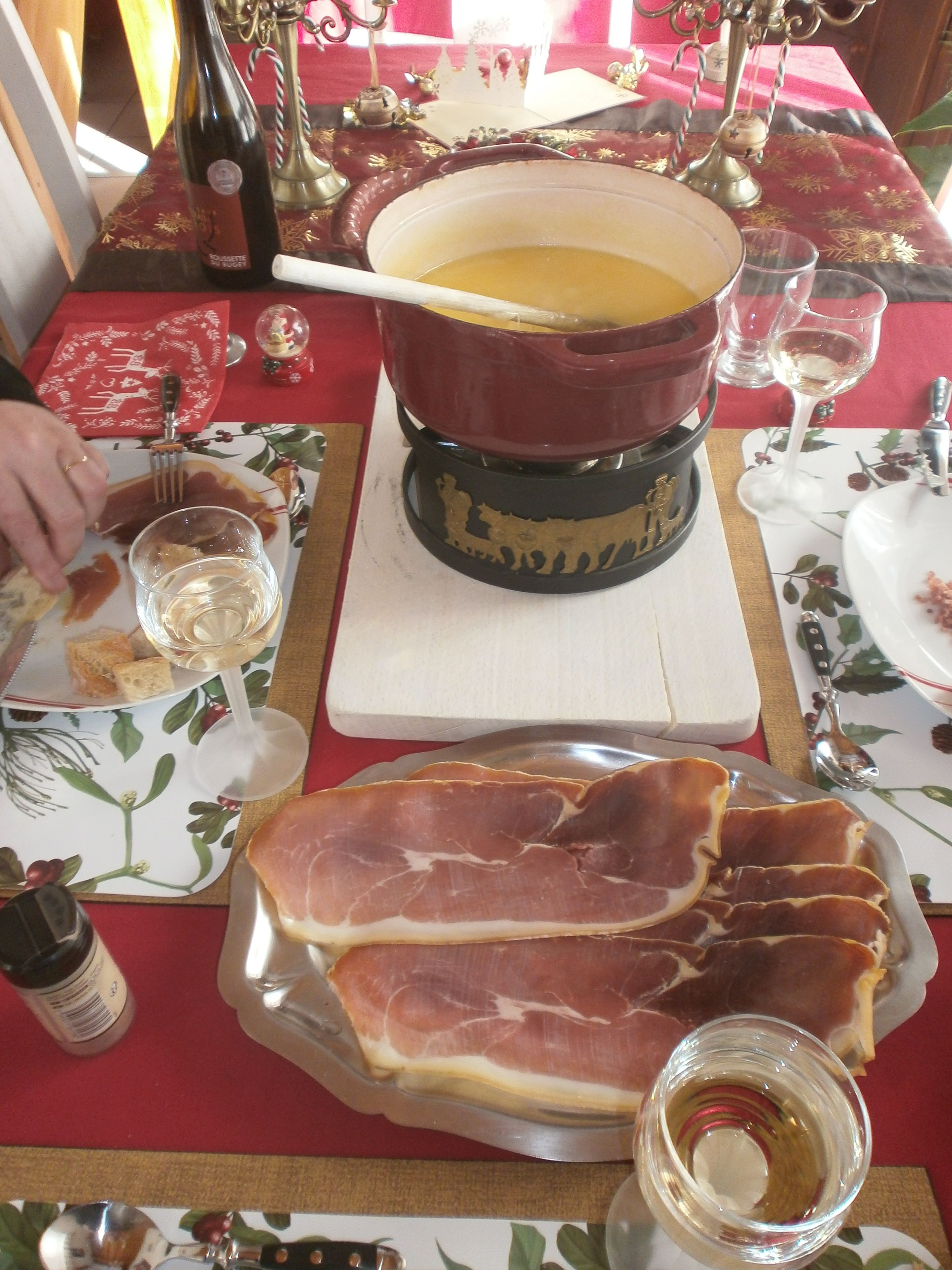 Une table à manger avec un pot de soupe, une assiette de jambon cru et une bouteille de vin.