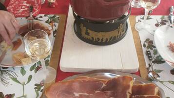 Une table à manger avec un pot de soupe, une assiette de jambon cru et une bouteille de vin.