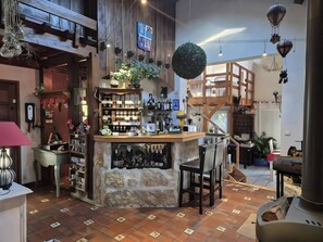Una zona de bar rústica con mostrador de piedra, estanterías con botellas y una escalera de madera.