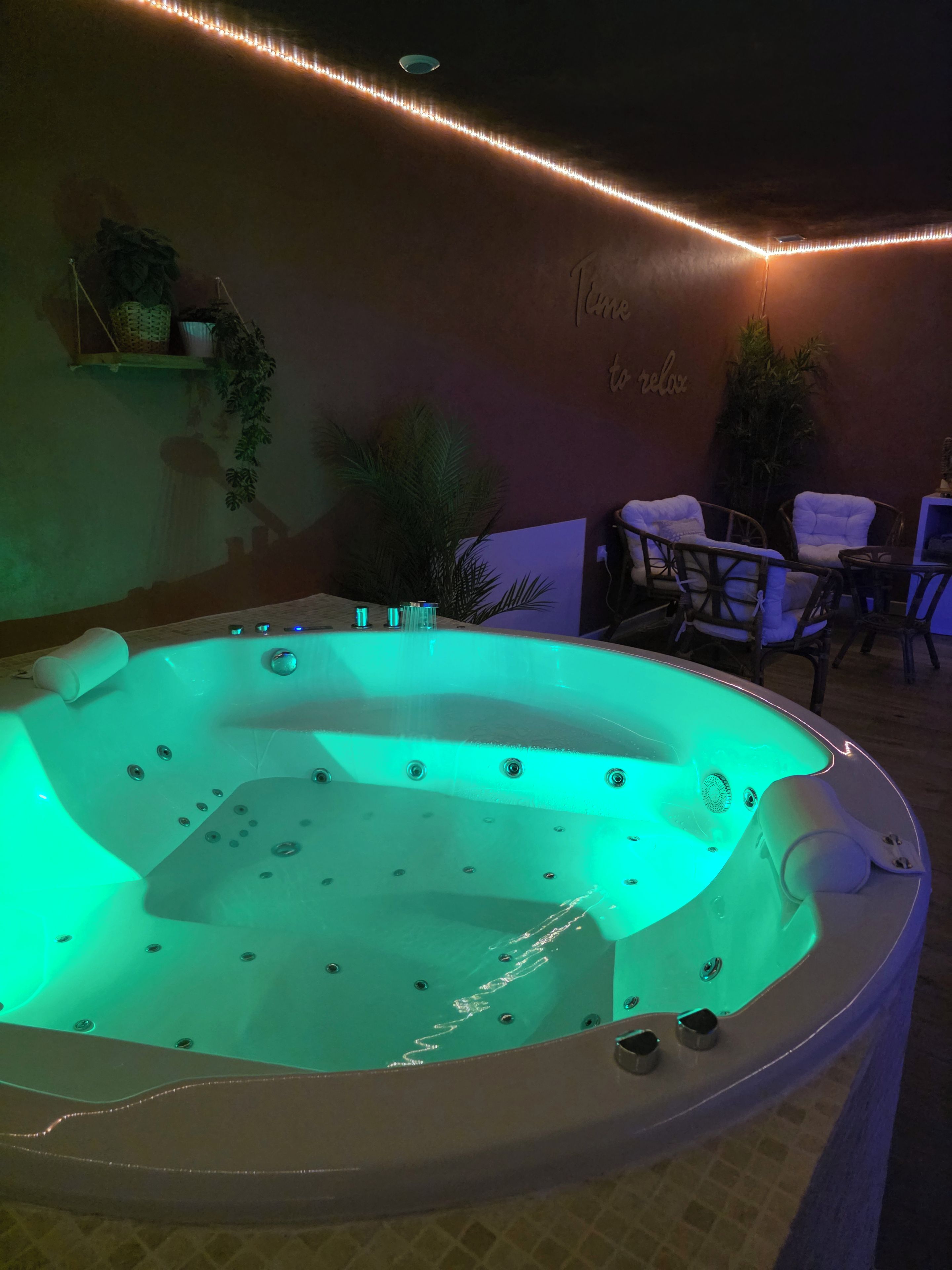 A hot tub with a green light, surrounded by chairs and tables, with a wall that has a 'Time to relax' sign.
