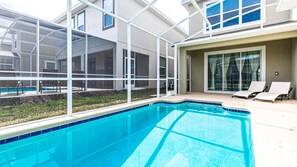 A swimming pool with a glass enclosure, lounge chairs, and a view of a building with large windows. - Family Villa w/ Themed Rooms, Pool & Resort Access (Davenport)