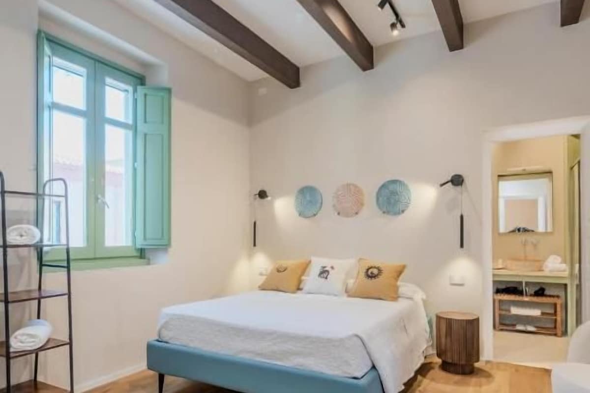 Quarto com cama, piso de madeira, janela e mesa de cabeceira.