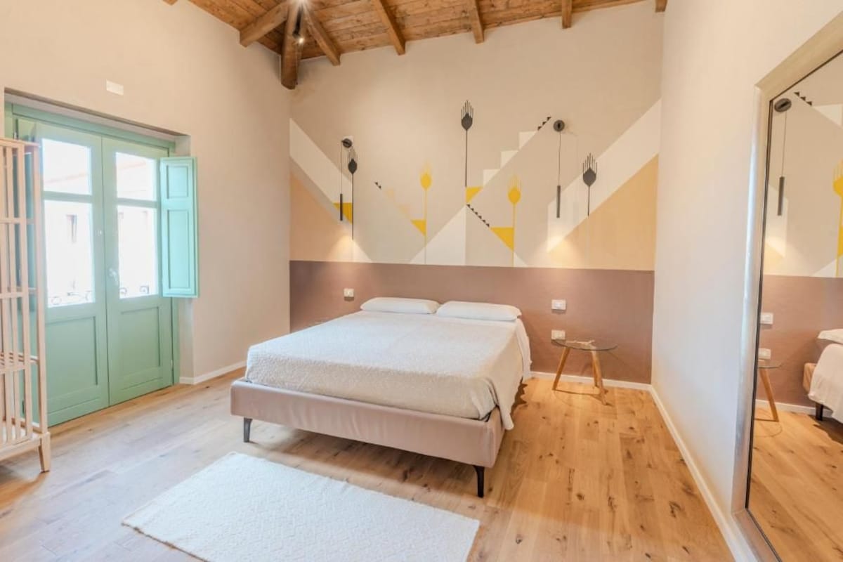 Quarto com cama, porta verde e parede com padrões geométricos.