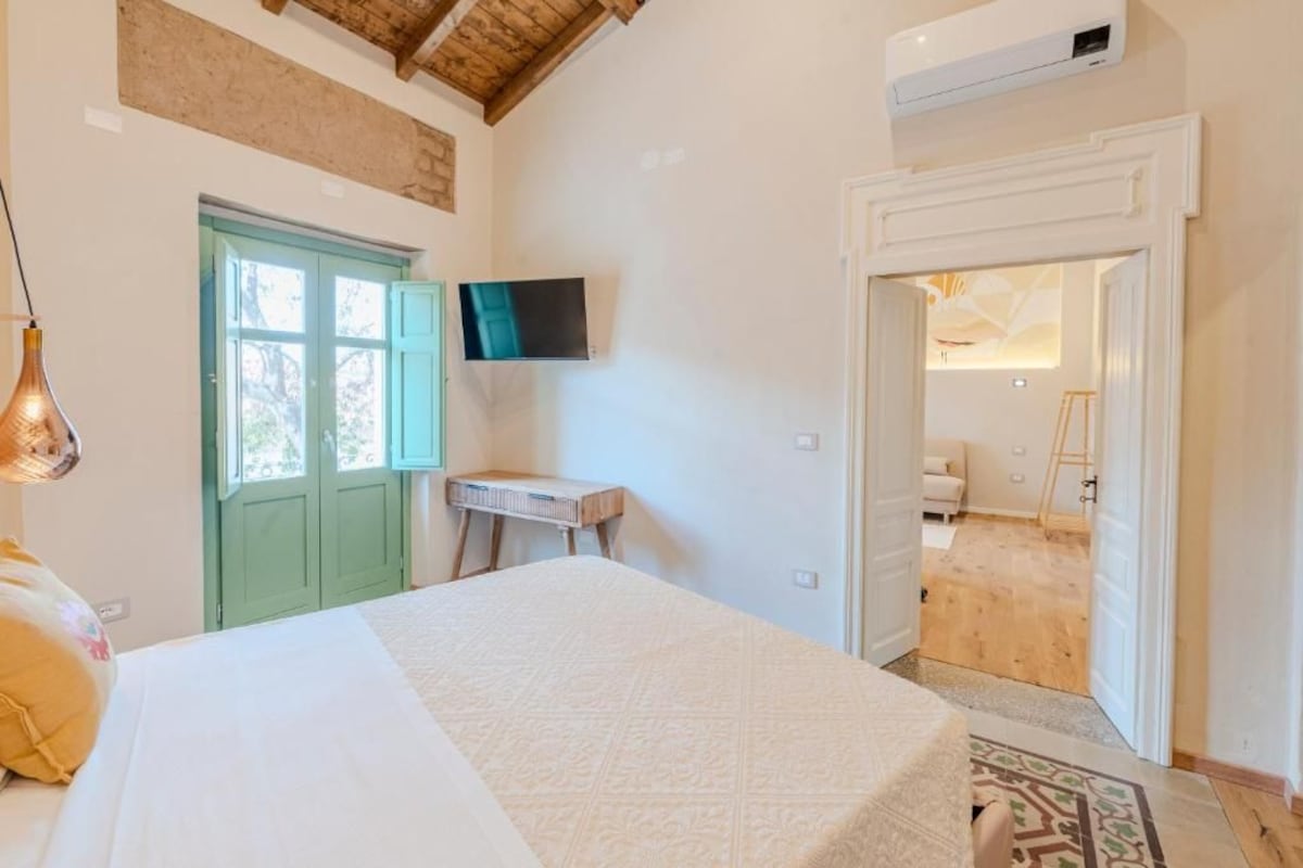 Quarto com cama, televisão, escrivaninha e porta para um banheiro.