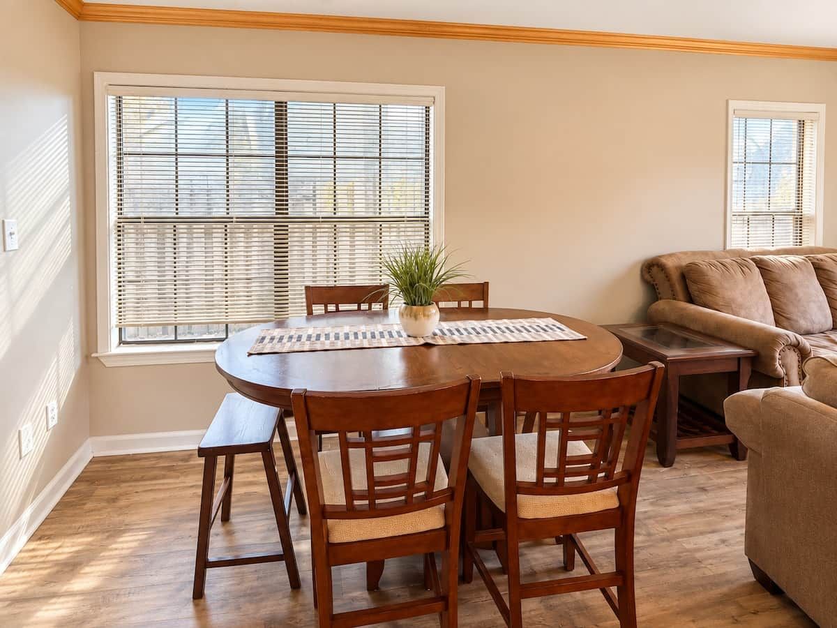 A dining area with a round table, wooden chairs, a potted plant, and a sofa.