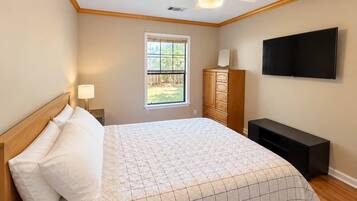 A bedroom with a bed, a nightstand, a dresser, a TV, and a window.