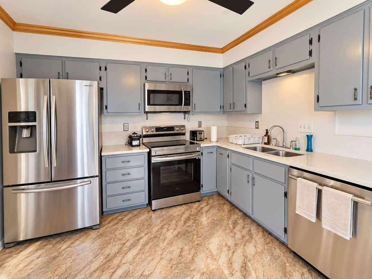 A modern kitchen with stainless steel appliances, grey cabinetry, and a marble floor.