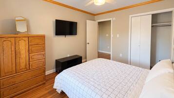 A bedroom with a bed, wooden dresser, TV, closet, and a ceiling fan.