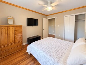 Ein Schlafzimmer mit Bett, einem Holzschrank, Fernseher, Kleiderschrank und Deckenventilator.