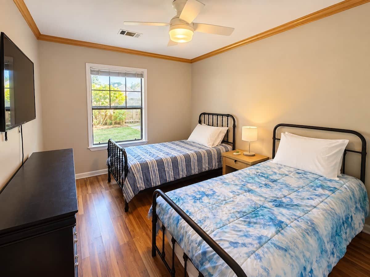 A bedroom with two beds, a ceiling fan, a window, and a TV.