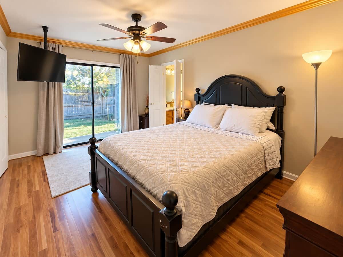 A bedroom with a bed, a TV, a ceiling fan, and a view of the outdoors.