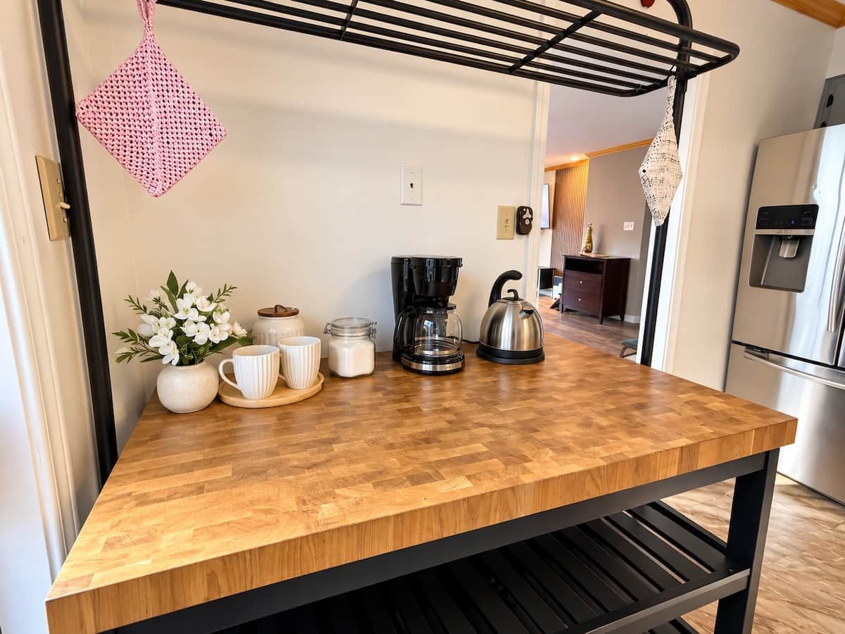 A kitchen with a wooden countertop, a coffee maker, a kettle, and a hanging pot rack.